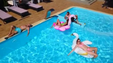 Havadan. Arkadaşlar şişme flamingo, kuğu, şamandıra ve şezlonglara bronzlaşırlar. Lüks otellerdeki şişme yataklarda banyo yapan mutlu gençler. Yukarıdan bak. Bikinili kızlar güneşte güneşleniyor.
