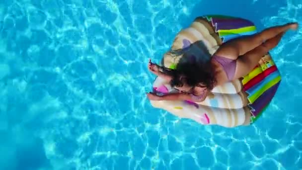 Z powietrza. Kobieta pływająca na dmuchanym materacu babeczkowym w basenie. Dziewczyna odpoczywa na platformie. Szczęśliwa młoda kobieta kąpie się z pływającą zabawką w luksusowym kurorcie. Widok z góry. Dziewczyna w bikini opalanie w słońcu. — Wideo stockowe