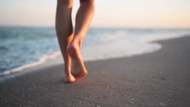 Smala kvinnliga ben och fötter som går längs havsvattenvågor på sandstranden. Vacker kvinna går vid havet surfa. Vattenstänk och skum i 120 fps slow motion. Flicka efter badande i havet går på stranden. — Stockvideo