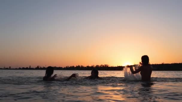 Felice ragazze bagnate silhouette in bikini divertirsi spruzzando acqua l'un l'altro al tramonto. Le amiche si divertono a fare spruzzi nello stagno all'alba. Le donne vanno a nuotare e fare il bagno nel lago al tramonto. Rallentatore — Video Stock