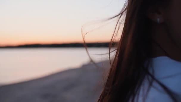 Закройте вид назад на нежное движение волос коричневой женщины в воздухе на летнем закате в замедленном режиме. Брюнетка или рыжая женщина, стоящая на беачи в сумерках. Ветер дует воздушные волосы, сияющие на рассвете. — стоковое видео