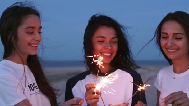 女性朋友们手握火花，散步，跳舞，在海滨的晚会上玩得很开心。年轻的少女在海滩上用烟火和灯笼狂欢。姑娘们动作慢，定时炸弹射中. — 图库视频影像