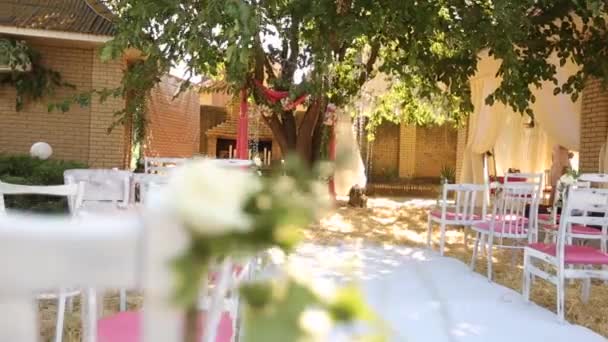 Úžasná rustikální výzdoba svatebního obřadu se senem, židlemi, květinářskými kompozicemi a svatebními šaty zavěšenými na stromě na pozadí. Letní krajina svatební koncept — Stock video