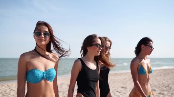 Grupo de amigas guapas divirtiéndose caminando por la playa tropical de arena en trajes de baño. Las mujeres interraciales charlando y riendo en el día de verano al aire libre. Chicas con bikini y trajes de baño junto al mar. — Vídeo de stock