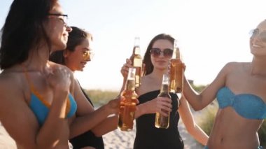 Bikinili güzel kadınlar gün batımında kumlu sahilde içki içerek ve dinlenerek eğleniyorlar. Mayolu kızlar, deniz kıyısında bira şişeleriyle asılı güneş gözlükleri. Genç dişiler limonata içer..