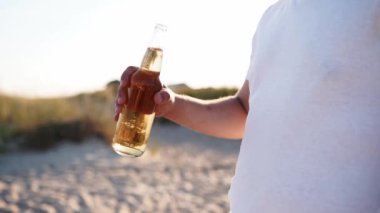 Gün batımında yavaş çekimde kumsalda cam şişe bira içen yakışıklı beyaz bir adam. Erkek, kumlu deniz kıyısında limonata ile susuzluğunu giderir. Güneş patlamaları, takip çekimi..