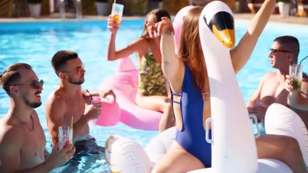 Amigos teniendo fiesta con cócteles en la piscina villa de vacaciones. Jóvenes felices en traje de baño bailando, bailando con flamenco inflable, cisne, colchón en un resort de lujo en un día soleado. Movimiento lento — Vídeo de stock