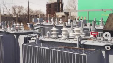 Elektrik dağıtım istasyonundaki güç transformatörü. Depoda ya da inşaat alanında yüksek voltajlı trafo var. Yalıtıcılar üzerindeki elektrik bağlantıları.