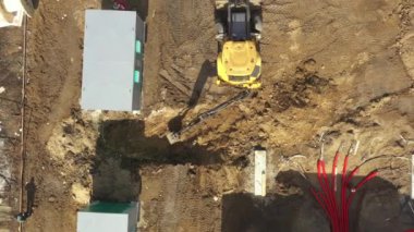 Güçlü sarı kazıcı havası kovayla çukur kazıyor. Yeraltı güç kablolarını kırmızı esnek çift katmanlı borularla döşemek. Construstion sitesine elektrik hatları kurulumu.