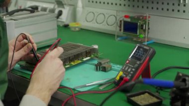 Teknisyen devre kartını çoklu metre ile test ediyor. Mühendis bitcoin ASIC madencisi PCB 'yi tamir ediyor. Çip lenslerinin yenilenmesi ve soğutma.