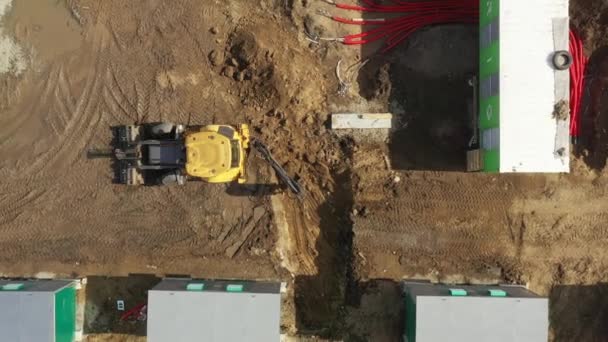 Antenn av kraftfull gul grävmaskin gräva dike med hink. Utläggning av underjordiska kraftkablar i röda flexibla dubbla korrugerade rör. Installation av elledningar på begränsningsplatsen. — Stockvideo