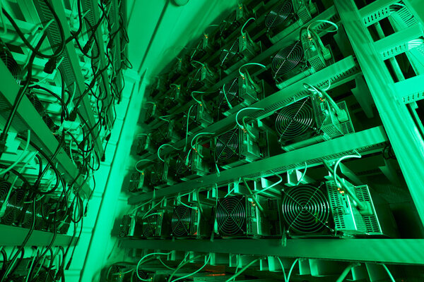 Bitcoin miners in large farm. ASIC mining equipment on stand racks mine cryptocurrency in steel container. Blockchain techology application specific integrated circuit datacenter. Server room lights.