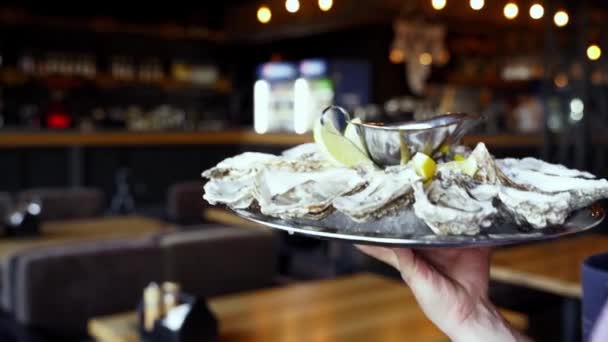 Servitören bär en bricka med serverade ostron på is med citron för lyxiga restaurangbesökare. Garcon ger salver stor tallrik traditionell meditarisk maträtt havet mat för finsmakare. — Stockvideo