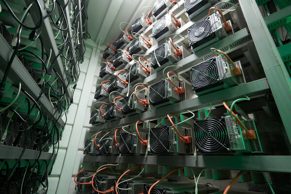 Bitcoin miners in large farm. ASIC mining equipment on stand racks mine cryptocurrency in steel container. Blockchain techology application specific integrated circuit datacenter. Server room lights.