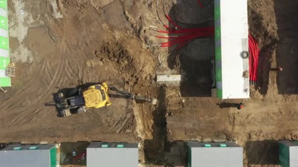 Antenn av kraftfull gul grävmaskin gräva dike med hink. Utläggning av underjordiska kraftkablar i röda flexibla dubbla korrugerade rör. Installation av elledningar på begränsningsplatsen. — Stockvideo