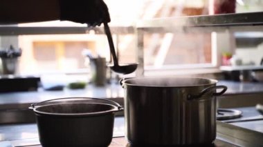 Aşçı yemek pişirirken çorba karıştırıyor ve kepçeyle balık kepçesi pişiriyor. Buhar tencereden yavaş çekimde çıkıyor. Aşçı restoran mutfağında buharlı tavalarla çalışır. Sağlıklı beslenme.