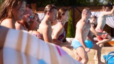 Lüks otellerde şişme şamandıralarla yüzme havuzunda zıplayan mutlu arkadaşlar. Mayolu gençler özel tatil köşkünde parti veriyorlar. Ateşli kızlar suya atlıyor. Yavaş çekim.