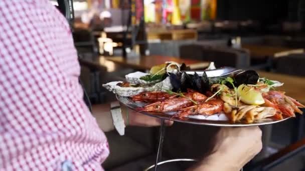 Waiters porta insieme frutti di mare misti, gamberetti aragosta, gamberetti re, cozze, ostriche e calamari serviti su un grande piatto di salver per i visitatori del ristorante di lusso. Garcon porta tradizionale piatto meditariano. — Video Stock