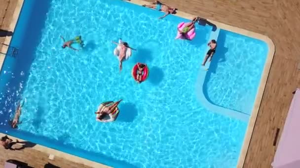 Z powietrza. Przyjaciele kładą opaleniznę na nadmuchiwanym flamingu, łabędziu, platformach i leżakach. Szczęśliwi młodzi ludzie kąpią się na materacach w luksusowym kurorcie. Widok z góry. Dziewczyny w bikini opalające się w słońcu — Wideo stockowe