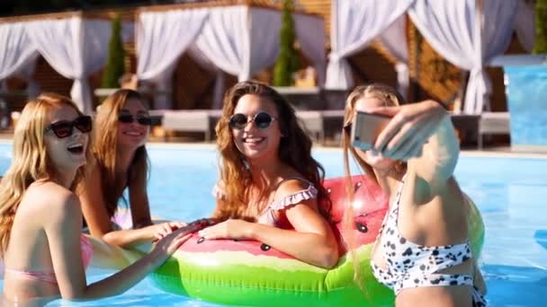 Schöne heiße hübsche Mädchen im Bikini machen Selfie im Schwimmbad auf aufblasbarer Wassermelone schwimmend. Fitte Frauen in Badebekleidung machen Fotos mit der Smartphone-Kamera auf einem Sommerfest an sonnigen Tagen. Zeitlupe — Stockvideo