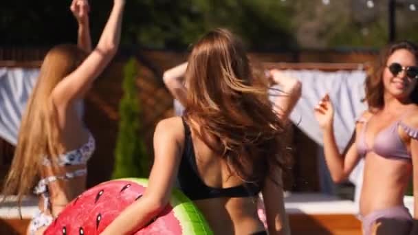 Hot pretty girls in bikini dancing with inflatable floaties by swimming pool. Attractive fitted women in swimsuits have fun relaxing, clubbing on sunny day summer party at luxury resort. Slow motion. — Stock Video