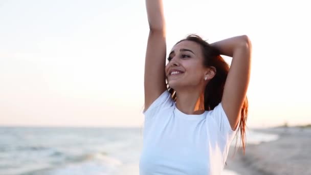 Mooie vrouw wandelen langs de kust op zandstrand plezier hebben met bierflesje. Aantrekkelijk ingericht meisje steekt de hand op, geniet van vrije tijd en zomervakantie in de buurt van de kust, drinken drank. Langzame beweging. — Stockvideo