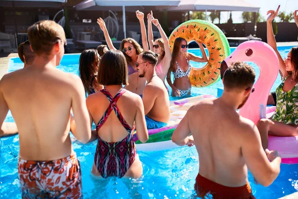 Multiracionális baráti társaság, akik egy privát villában buliznak. Boldog fiatalok fürdőruhában táncolnak és buliznak felfújható flamingóval, hattyúval, úszógyűrűvel luxus üdülőhelyen a napsütéses napon. — Stock Fotó