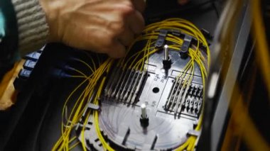 İşçi, bağlantı kutusunda optik hat internet kablosu bağlıyor. Servis elemanı optik fiber lehim yapıyor. Optik fiber ve yönlendirici kablolarıyla sunucu odasında çalışan internet servis sağlayıcısı mühendisi..