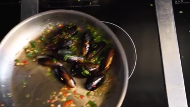 Cuisson de délicieuses moules fraîches sur une poêle chaude dans un restaurant de luxe. Le chef secoue et mélange les moules et les légumes sur un gril. Cuisine méditerranéenne traditionnelle. Scène de ralenti. — Video