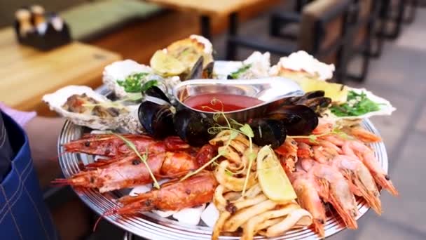 Waiters carries mixed seafood set, lobster shrimp, king prawns, mussels, oysters and squids served on large salver plate for luxury restaurant visitors. Garcon brings traditional meditarian dish. — Stock Video