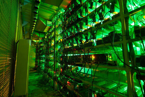 Bitcoin miners in large farm. ASIC mining equipment on stand racks mine cryptocurrency in steel container. Blockchain techology application specific integrated circuit datacenter. Server room lights.