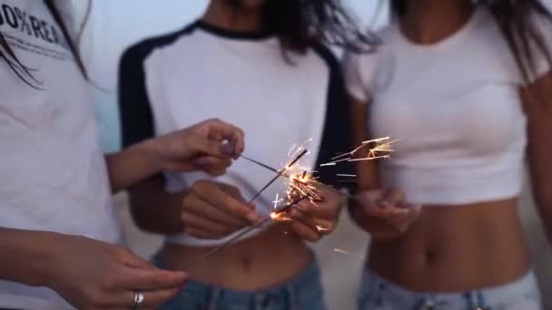 Amici donne che camminano, ballano, si divertono alla festa notturna al mare con scintille in mano. Giovani adolescenti che festeggiano sulla spiaggia con fuochi d'artificio, luci del bengala. Ragazze al rallentatore, colpo steadycam. — Video Stock