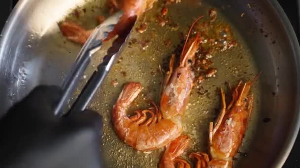 Cook förvandlar räkor med pincett på en grill. Närbild av kung räkor steka i en panna. Kocken steker kungliga räkor på en varm stekpanna. Makrohavsberedning av livsmedel. — Stockvideo