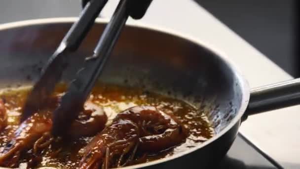 Cook convierte los camarones con fórceps en una parrilla. Primer plano de langostinos fritos en una sartén. Chef freír camarones reales en una sartén caliente. Preparación de alimentos de mar macro. — Vídeo de stock