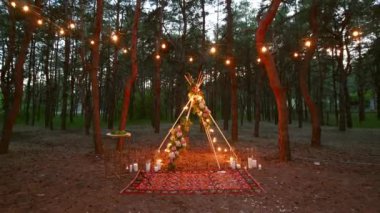 Çam ormanlarındaki açık hava düğün mekanında boho tipi kemer dekoru aydınlatması. Yazın kırsal düğünlerde sandalyelerin üzerinde parlayan eski sicim lambaları, çelenkler..