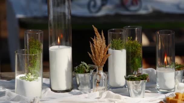 Banquet de mariage en plein air en forêt. Table à manger décorée dans le style boho avec des bougies, tissu blanc, fleurs, servi avec des assiettes, vaisselle, plats, repas, couverts et boissons. Restauration vacances. — Video