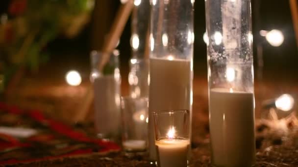 Свечи, горящие в стеклянных вазах, фляжки на ковре возле богемной арки типи, украшенные розами и цветами, завернутыми в сказочные огни на открытой свадебной церемонии в сосновом лесу. Бохо деревенский декор. — стоковое видео