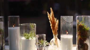 Düğün partisi dışarıda ormanda ziyafet veriyor. Mum, beyaz kumaş, çiçek, tabak, sofra takımı, yemek takımı, yemek takımı, kadeh ve içeceklerle süslenmiş yemek masası. Tatil yemekleri..