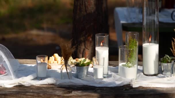 Banquete de boda al aire libre en el bosque. Mesa de comedor decorada en estilo boho con velas, tela blanca, flores, servida con platos, vajilla, platos, comidas, copas y bebidas. catering de vacaciones. — Vídeos de Stock