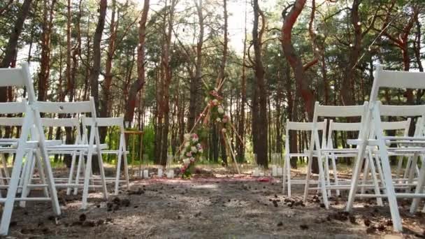 Vacker bohemisk tipi båge dekoration på utomhus bröllop plats i tallskog med kottar. Stolar, blommiga blomsterkompositioner av rosor, matta, sträng älva ljus. Sommarbröllop på landsbygden. — Stockvideo