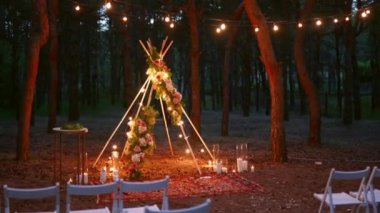Çam ormanlarındaki açık hava düğün mekanında boho tipi kemer dekoru aydınlatması. Yazın kırsal düğünlerde sandalyelerin üzerinde parlayan eski sicim lambaları, çelenkler..