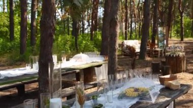 Çam ormanında düğün ziyafeti. Yemek masaları, mum, çiçek, bahar perisi ışıkları, tabaklar, şarap kadehleri, ahşap çerçevelerle süslenmiş banklar. Çevresel organik çiçek dekoru.