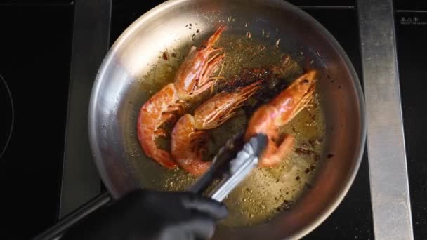Cook γυρίζει γαρίδες με λαβίδα σε μια σχάρα. Κοντινό πλάνο του βασιλιά γαρίδες τηγάνισμα σε ένα τηγάνι. Ο σεφ τηγανίζει βασιλικές γαρίδες σε καυτό τηγάνι. Προετοιμασία μακρο-θαλασσινών τροφίμων. — Αρχείο Βίντεο