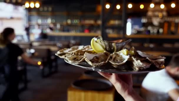 Serveur porte un plateau d'huîtres servies sur glace avec du citron pour les visiteurs du restaurant de luxe. Garcon apporte salver grande assiette plat méditarien traditionnel fruits de mer pour les gourmets. — Video