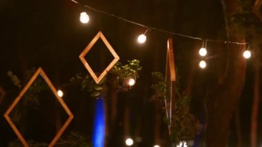Çiçekli ahşap çerçeveler Boho tarzı düğün mekânında asılı, çam ormanında, ipe bağlı ışıklar ve gece lambasıyla. Ülke ya da kırsal organik dekor.