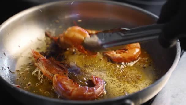 Cook convierte los camarones con fórceps en una parrilla. Primer plano de langostinos fritos en una sartén. Chef freír camarones reales en una sartén caliente. Preparación de alimentos de mar macro. — Vídeo de stock