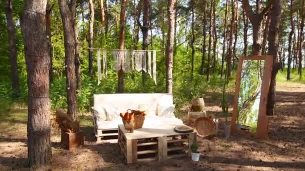 Loş kanepeli fotoğraf odası ve çam ormanlarındaki açık hava düğün mekanında boho stili kargo paletleri masası. Bohem dekor. — Stok video