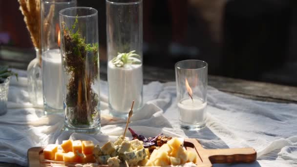 Γαμήλια δεξίωση έξω στο δάσος. Τραπεζαρία διακοσμημένη σε boho στυλ με κεριά, λευκό πανί, λουλούδια, σερβίρεται με πιάτα, επιτραπέζια σκεύη, πιάτα, γεύματα, ποτήρια και ποτά. Εστίαση διακοπών. — Αρχείο Βίντεο