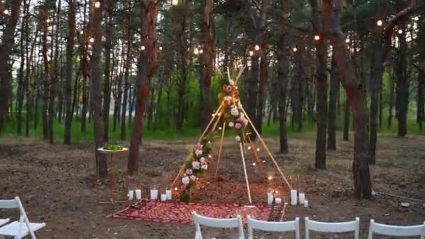 Праздничная подсветка струнных огней на арке Boho tipi на открытой свадебной церемонии в сосновом лесу ночью. Винтажные лампочки лампочки гирлянды лампы сияют над стульями на летней сельской свадьбе. — стоковое видео