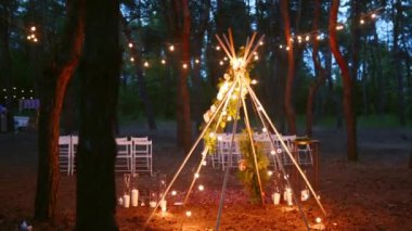 Çam ormanlarındaki açık hava düğün mekanında boho tipi kemer dekoru aydınlatması. Yazın kırsal düğünlerde sandalyelerin üzerinde parlayan eski sicim lambaları, çelenkler..